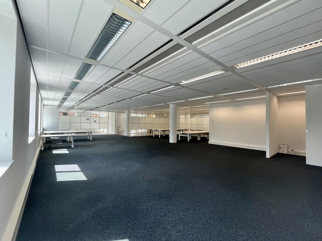 Spacious and empty office space with desks and large windows at Koningin Wilhelminaplein.